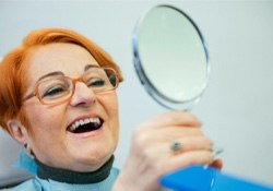 An elderly woman admiring her dentures in a hand mirror