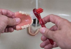 Someone cleaning dentures with a toothbrush