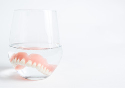 A closeup of dentures soaking in a glass