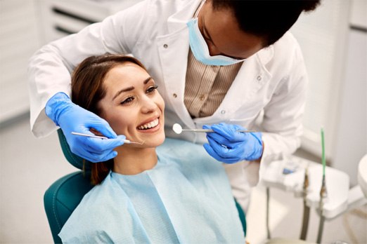 Dentist leaning over patient with instruments to examine her mouth