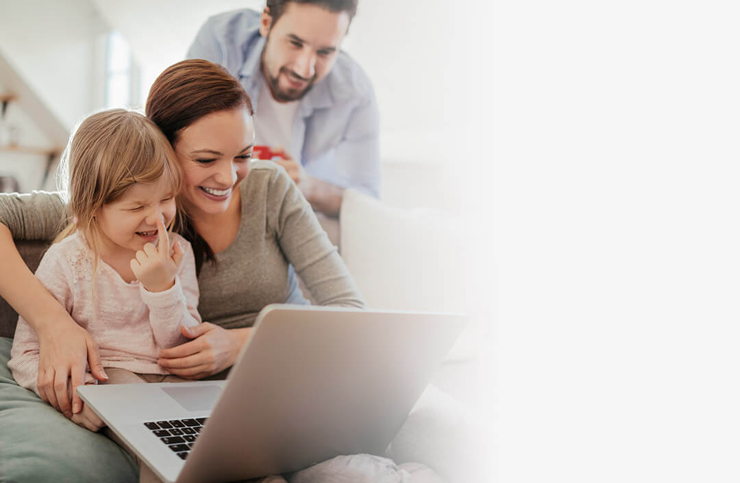 Woman and daughter sitting on couch and looking at laptop