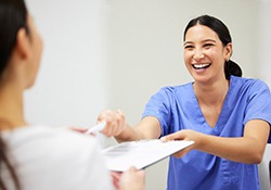 A dental assistant handing a patient a dental insurance form