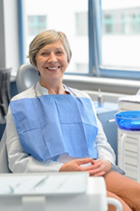 Woman sitting in dentist chair smiling and wearing a dental bib