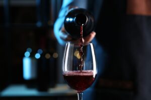 Someone pouring glass of red wine.